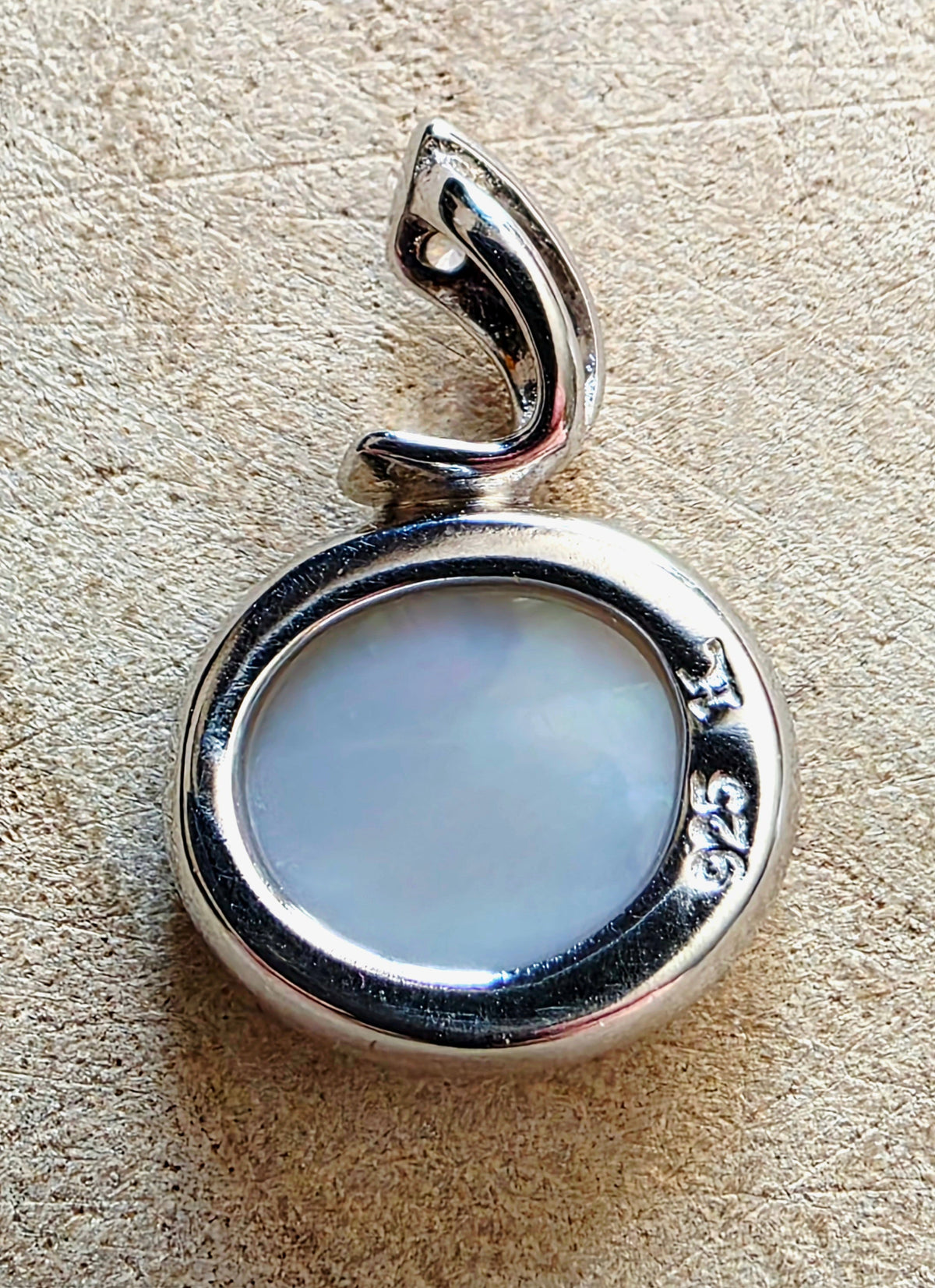 A sterling silver pendant with a polished oval frame and a smooth, milky white opal, resting on a textured beige surface.