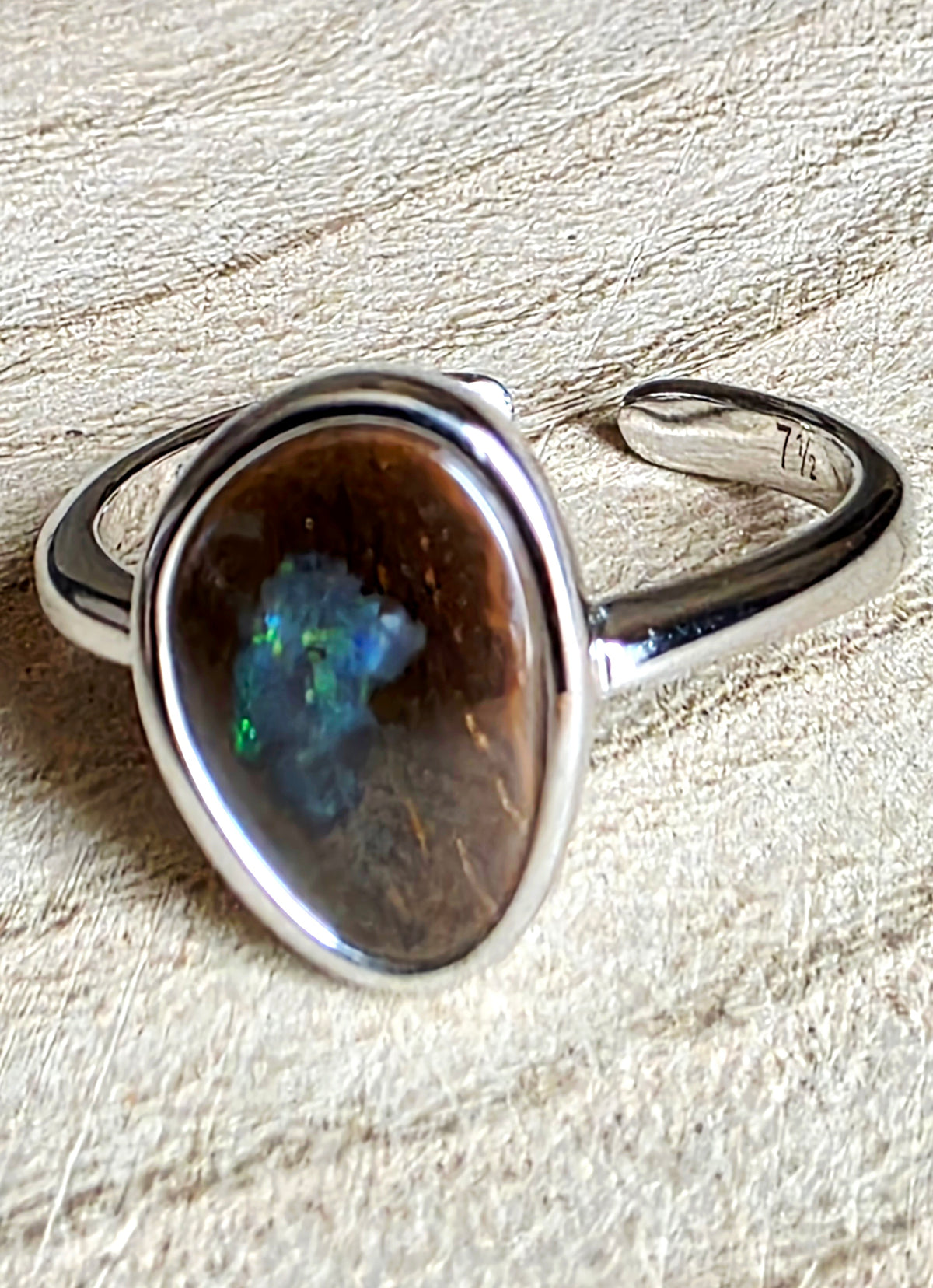 A silver ring featuring a large, oval-shaped opal gemstone with vibrant blue and green flashes, resting on a textured beige fabric background.