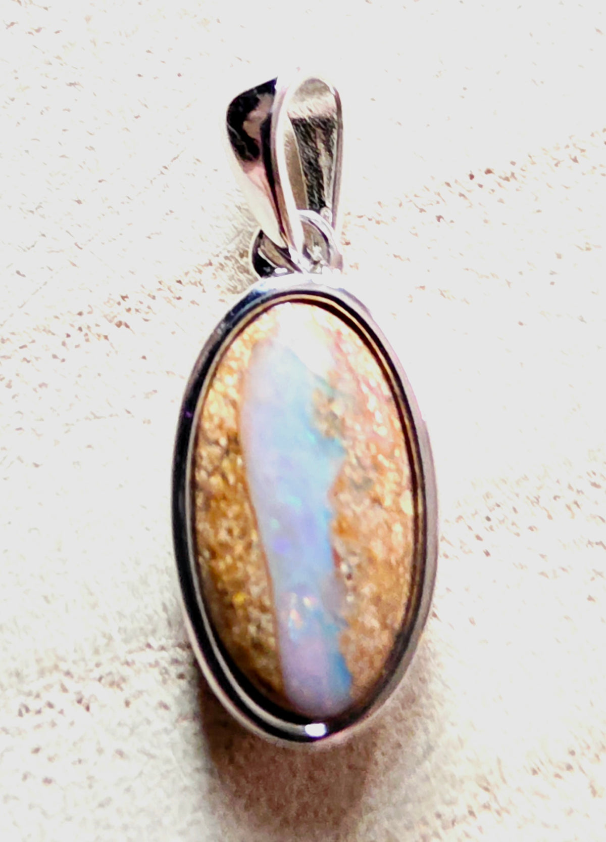 An oval pendant featuring a natural opal stone with iridescent blue, white, and gold patterns, set in a polished silver bezel with a matching bail.