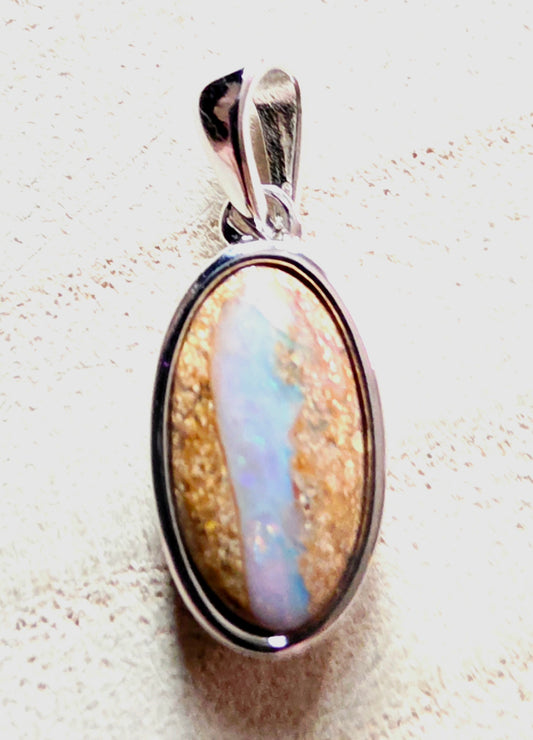An oval pendant featuring a natural opal stone with iridescent blue, white, and gold patterns, set in a polished silver bezel with a matching bail.