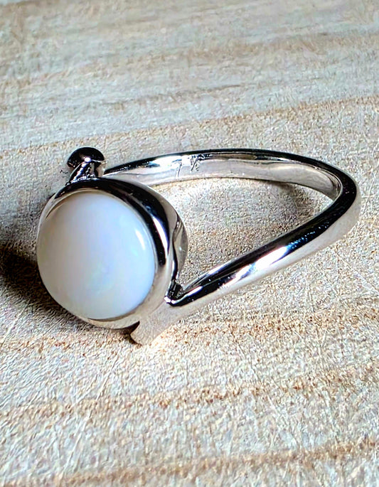 A silver ring with a large, round, iridescent crystal opal cabochon, resting on a textured beige background.