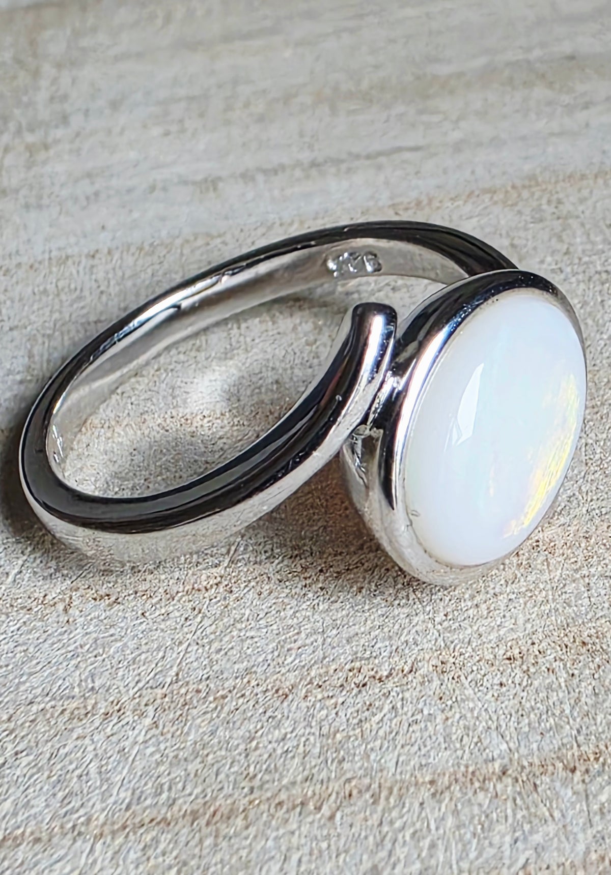 A sterling silver ring with a large, oval, milky white cabochon opal, resting on a textured beige background.