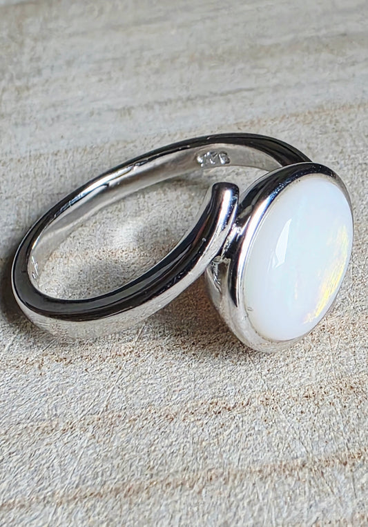 A sterling silver ring with a large, oval, milky white cabochon opal, resting on a textured beige background.