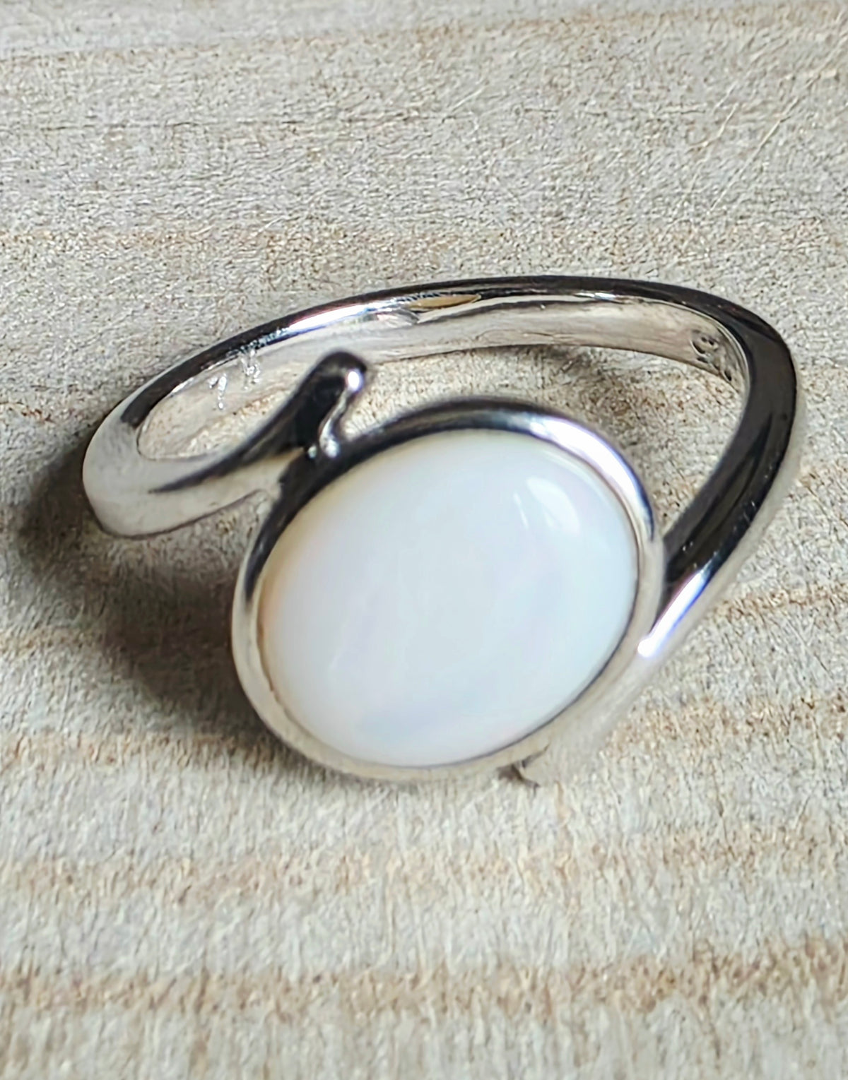 A sterling silver open-band ring featuring a large, smooth, oval white cabochon opal, photographed on a textured beige background.