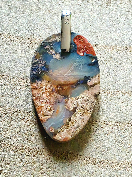 A teardrop-shaped pendant made from polished opal with swirling patterns of blue, beige, brown, and rust orange, featuring a silver bail