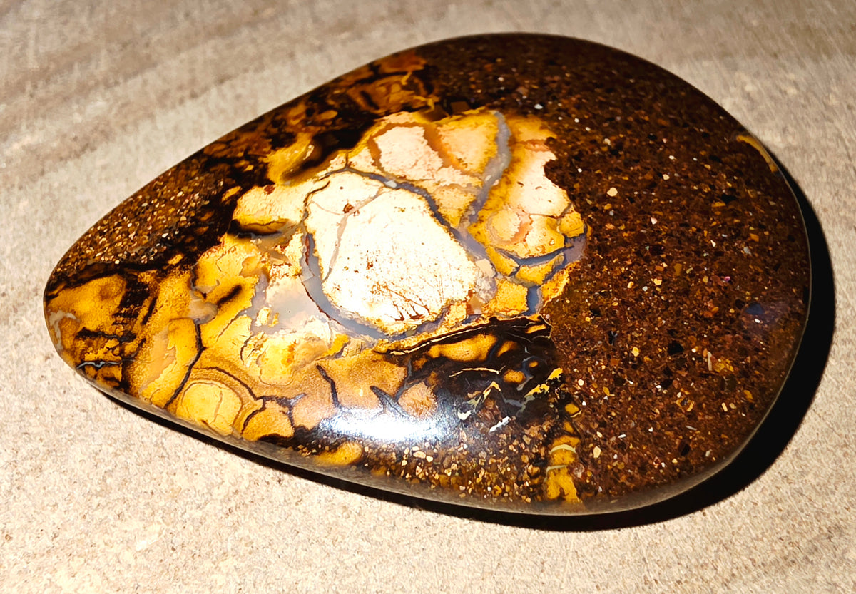 A polished brown and gold boulder stone with a prominent cream-coloured central matrix, resting on a textured beige surface.