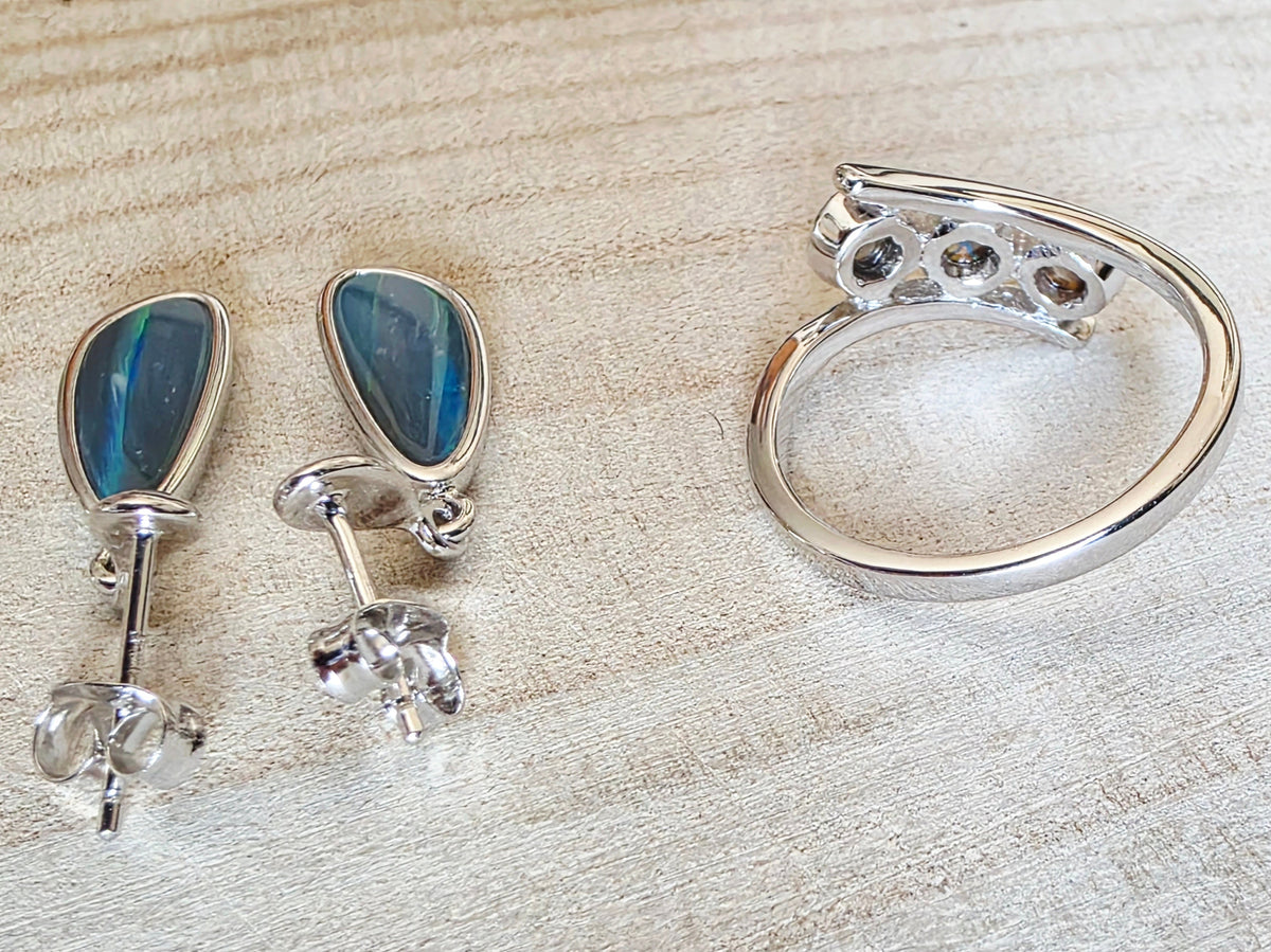 A sterling silver jewellery set featuring a curved huggie ring and matching drop earrings with teardrop-shaped blue iridescent opal stones, displayed on a light wood surface.