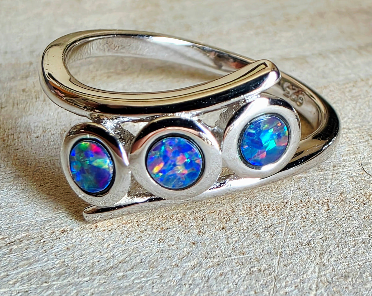 A sterling silver ring with three round, colourful opal gemstones, displayed on a textured beige surface.