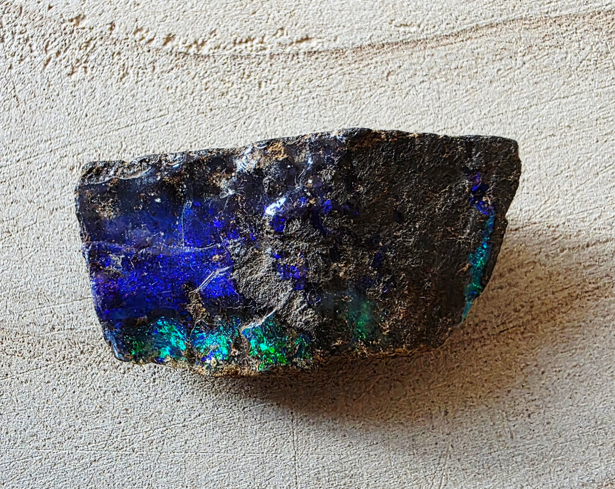 A raw opal opal specimen with vibrant blue and green iridescent play-of-colour on a textured beige background.