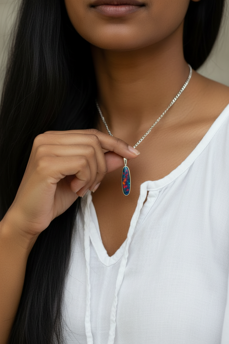 A close-up of a woman wearing a silver chain necklace with a teardrop-shaped pendant featuring a colourful opal pattern of red, blue, and green, paired with a white top.